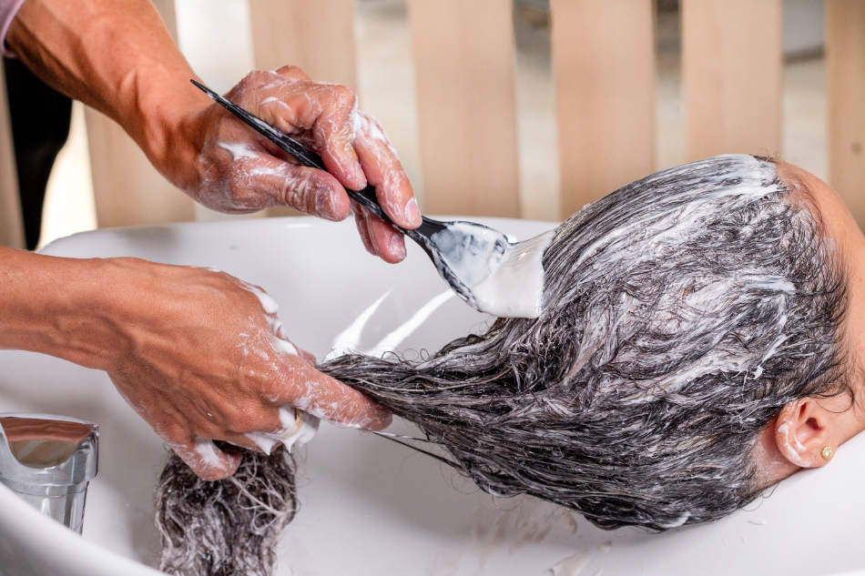 Sustainable hair foils: Professional artist applying dye with a brush on a woman's curly hair. Professional beauty salon.